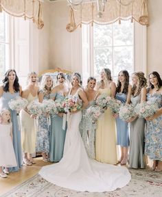 a group of women standing next to each other in front of a window holding bouquets