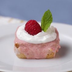 a small dessert on a white plate with a raspberry and whipped cream topping