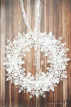 a white snowflake wreath hanging on a wooden wall with ribbon and string attached to it