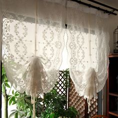 two white curtains hanging from the side of a window next to a potted plant