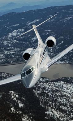 an airplane flying in the air over snow covered mountains and trees, with its landing gear down