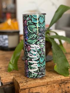 a green plant sitting on top of a wooden table next to a metal canister