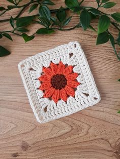 a crocheted square with an orange and brown flower in the center on a wooden surface