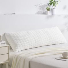 there is a white bed with pillows on it and a plant next to the bed