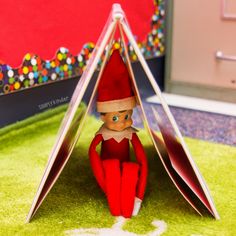 an elf is sitting in the corner of a room with green carpet and red walls