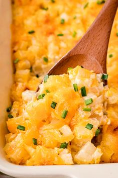 a wooden spoon in a casserole dish filled with potatoes and chicken, garnished with scallions