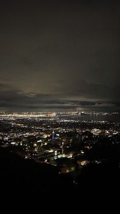 the city lights are lit up in the dark night sky over an area with hills and trees