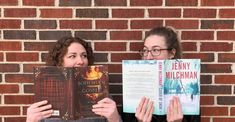 two women holding up books in front of a brick wall