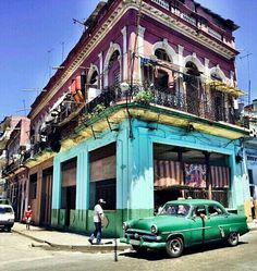 an old green car parked in front of a building with balconies on it