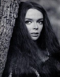 a woman with long hair standing next to a tree