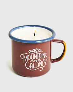 the mountains are calling candle is sitting in a red cup with blue rim and handle