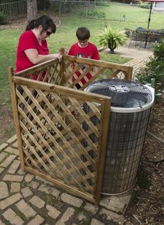 a woman and boy are looking at an air conditioner outside in the yard,