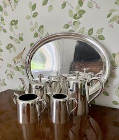 a group of silver teapots sitting on top of a wooden table next to a mirror