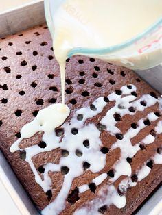 a person pouring milk on top of a brown cake in a pan with holes and white icing