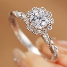 a woman's hand holding an engagement ring with a flower design on the side