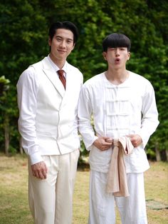 two young men in white suits standing next to each other on the grass with trees in the background