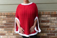 a woman standing in front of a brick wall wearing a red and white crocheted ponchy