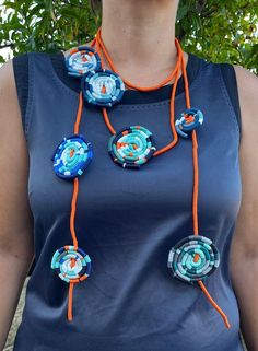 a woman wearing an orange and blue necklace with flowers on it's end, standing in front of a tree