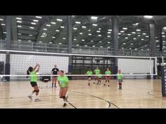 some people are playing volleyball in an indoor court with lights on and one person is reaching up to hit the ball