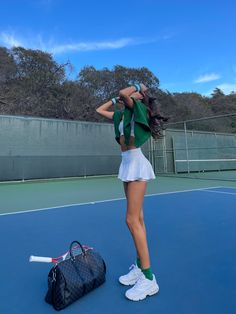 a woman standing on top of a tennis court holding a racquet next to a bag