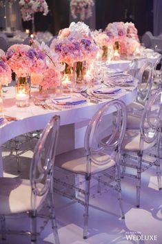 the table is set with clear chairs and pink flowers in vases on each side