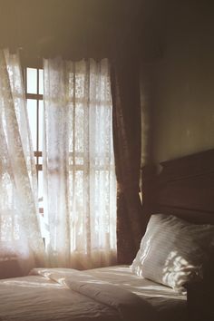 the sun shines through the sheered curtains on a bed in front of a window