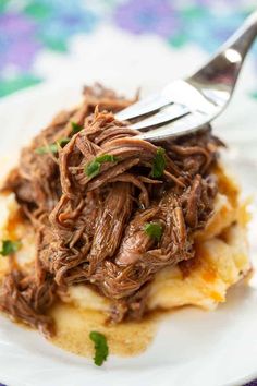 a white plate topped with meat and potatoes covered in gravy on top of mashed potatoes