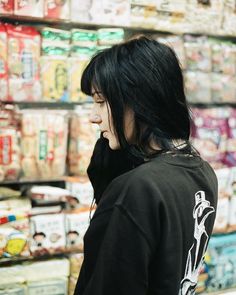 a man with long black hair standing in front of a store filled with food items