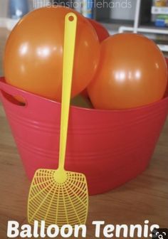 an orange and yellow ball in a red bucket with a rake on it that says balloon tennis