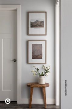 three framed pictures hang on the wall next to a small table with flowers in it