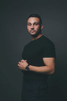 a man standing in front of a black background with his arms crossed and looking at the camera