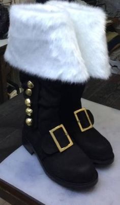 a pair of black boots with white fur and gold buckles on the side, sitting on top of a table