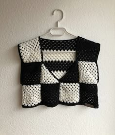 a black and white crocheted vest hanging on a wall