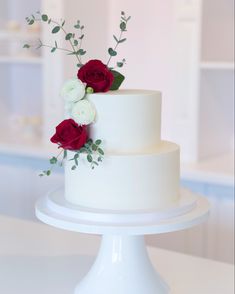 a three tiered white cake with red and white flowers on the top, along with greenery