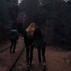 two people walking on train tracks in the woods at night, one carrying a backpack