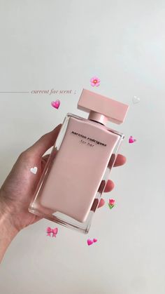 a person's hand holding a pink perfume bottle in front of a white background