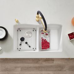 two white sinks with black handles and red berries in the bottom left hand drainer