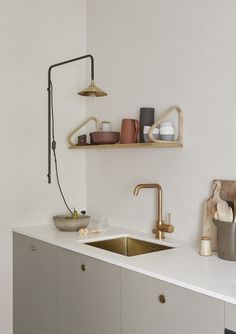 a kitchen with white walls and gold faucets on the counter top, along with wooden shelves