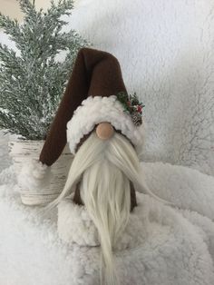 a gnome with white hair and a brown hat is sitting in the snow next to a potted plant