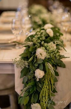 the table is set with white flowers and greenery for an elegant touch to it