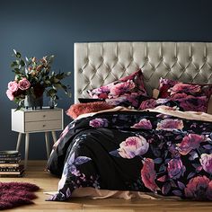 a bedroom with blue walls and pink flowers on the bedspread, along with an upholstered headboard