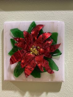 a red and green glass flower sitting on top of a white wall