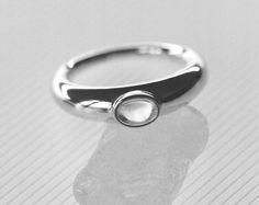 A punctuating 4x6mm oval quartz cabochon stone, bezel set on a graduated and full round solid band.The Glacé Ring I is part of our classic Glacé Collection, pairing solid, 100% recycled 14k gold or sterling silver with clear quartz; equal parts modern statement and a relic that could belong to any era. Exploring the limits of shape through our signature lens of timelessness and wearability, our Glacé collection includes both our permanent clear quartz styles and evolving capsules incorporating l Modern Jewelry With Bezel Set Oval Cabochon, Modern Jewelry With Oval Cabochon Bezel Setting, Classic Oval Cabochon Ring With Smooth Bezel, Timeless Oval Moonstone Ring With Polished Finish, Modern Moonstone Ring With Oval Bezel Setting, Oval Modern Moonstone Ring With Bezel Setting, Modern Oval Moonstone Ring With Bezel Setting, Modern Domed Ring With Bezel Setting, Modern Moonstone Ring With Oval Cabochon