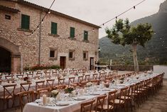 tables set up for an outdoor wedding reception in front of a stone building with green shutters