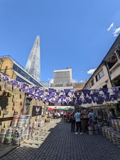 people are walking through an outdoor market with purple and white flags hanging from the buildings