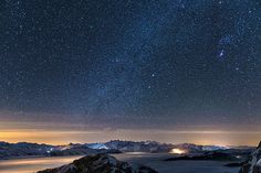 the night sky is filled with stars above some snow covered mountains and water in the foreground