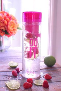 a pink water bottle sitting on top of a wooden table next to raspberries and limes