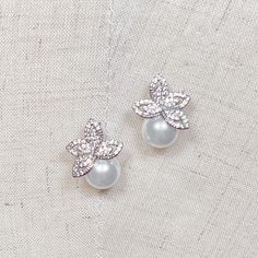 pair of pearl and crystal flower earrings on white fabric background, closeup view from above