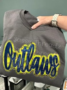 someone is holding up a sweatshirt with the word outlands on it in blue and yellow