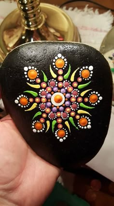 a hand holding a painted rock in the shape of a flower